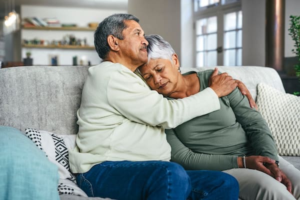 Photo of a couple embracing on a couch, looking serious, perhaps dealing with a diagnosis of Major Depressive Disorder