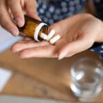The question who takes antidepressants represented by hands pouring pills out of a bottle