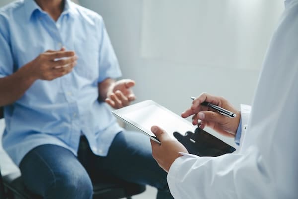 TRD Research represented by a person in a white coat holding a clipboard and talking to a patient.